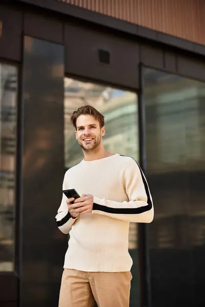 Un bell'uomo passeggia attraverso un moderno paesaggio urbano, godendo della luce del giorno mentre usa il suo telefono. — Foto stock