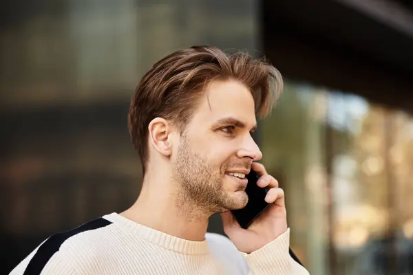 Un bell'uomo cammina in una città affollata, chiacchierando al telefono con un sorriso luminoso. — Foto stock