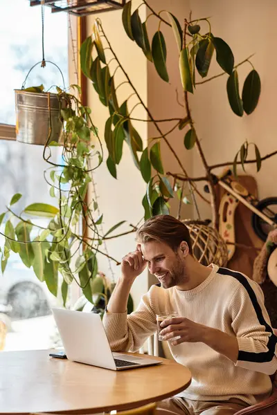 A handsome man relaxes with a drink, focused on his laptop in a warmly decorated cafe. — Stock Photo