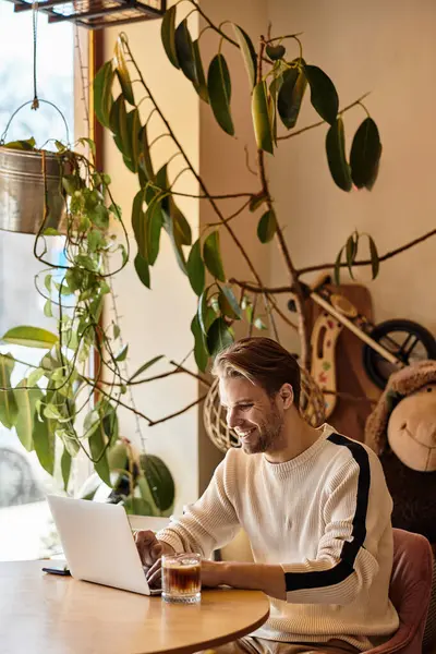 A handsome man works intently on his laptop while sipping a drink in a welcoming cafe atmosphere. — Stock Photo