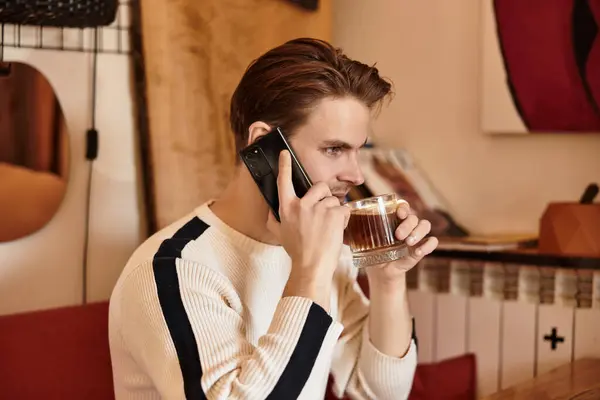 A stylish young man sips coffee and chats on his phone in a cozy cafe. — Stock Photo