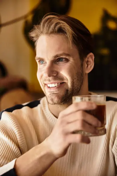 Handsome man smiles warmly while holding a drink in a trendy cafe, capturing a moment of joy. — Stock Photo