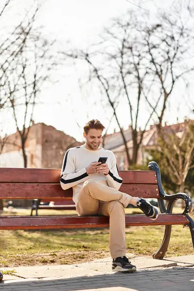 Gut gelaunter Mann geht durch einen belebten Park, in sein Smartphone vertieft, inmitten einer wunderschönen Landschaft. — Stockfoto