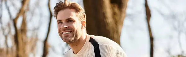 A charming man walks confidently, smiling in a vibrant park on a bright day, exuding joy. — Stock Photo
