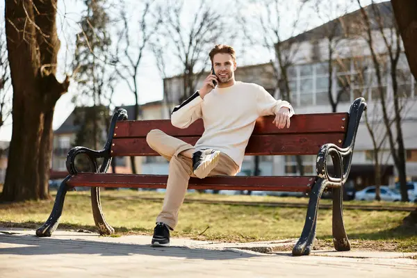 Bright day in a lively park with a handsome man walking and happily talking on his phone. — Stock Photo