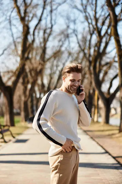 A dapper man enjoys a walk in the park, smiling as he talks on the phone on a sunny day. — Stock Photo