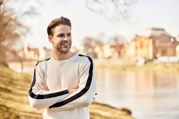 A handsome man strolls along the riverbank, smiling as he enjoys the warm sunshine of springtime. — Stock Photo