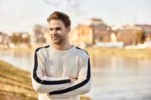 A stylish young man strolls by the river, enjoying the warm sunlight and serene surroundings. — Stock Photo