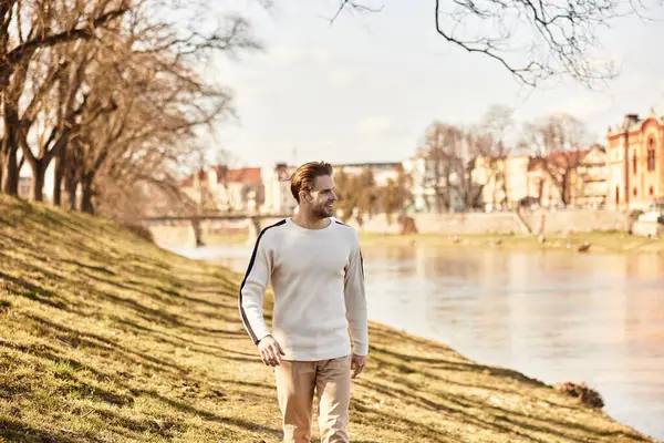 A handsome man enjoys a leisurely walk along the riverbank, soaking in the warm afternoon sun. — Stock Photo