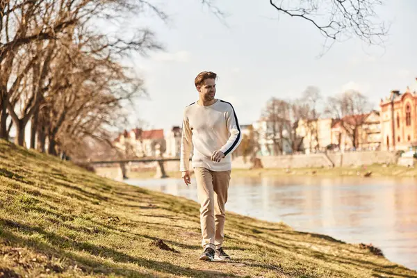 A dapper gentleman enjoys a leisurely walk beside a tranquil river, embodying relaxation and charm. — Stock Photo