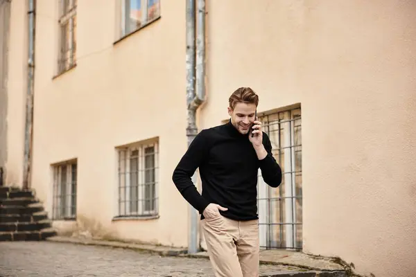 A confident man strolls along a quaint street, engaged in a phone conversation, exuding charm. — Stock Photo