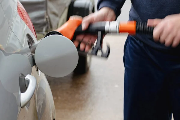 Man refueling a car in Europe with a pistol in his hand. Gas station - refueling, diesel and gasoline. The man fills a tank of a silver car with fuel