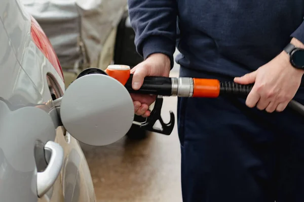 Man refueling a car in Europe with a pistol in his hand. Gas station - refueling, diesel and gasoline. The man fills a tank of a silver car with fuel