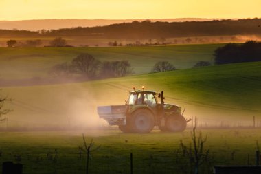 Tractor in farmland working on soil field with sunset, big equipment, countryside scene