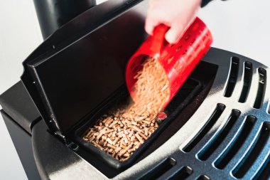 Close-up on pellets, black domestic pellet stove, man loading by hand granules with a red 3 d printed cup