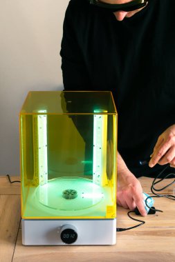 3 boyutlu reçine yazıcısı için ultraviyole ışığı kullanan gözlüklü bir adam çamaşır makinesini ayarlıyor.