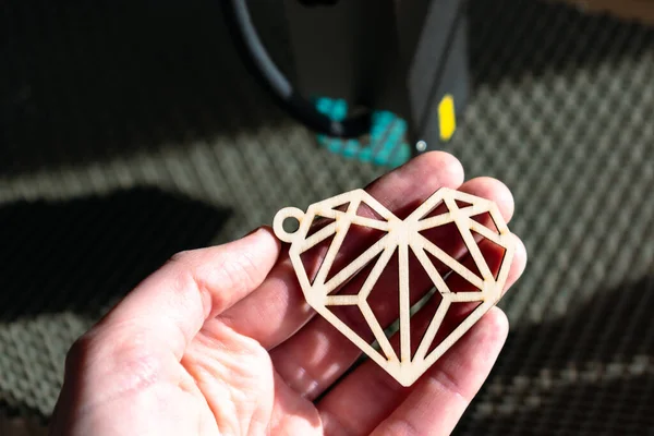 Laser engraving and cutting, hand holding an example of a cut out wooden heart