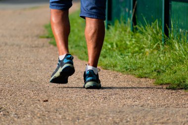 Yolunda spor ayakkabılarla yürüyen bir adam, bacaklarına yakın çekim, spor aktivitesi, sağlıklı yaşam tarzı