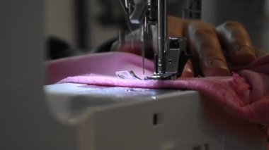 Pembe kumaşa dikiş atmak için dikiş makinesi kullanan bir adam.