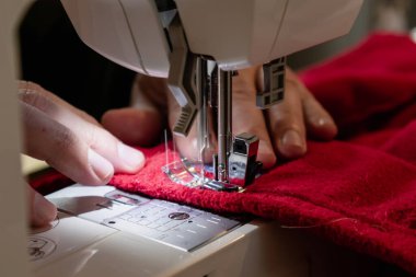 Kırmızı giysili bir dikiş makinesi kullanan bir adam. Tamir, kişiselleştirme, yaratma, yükseltme.