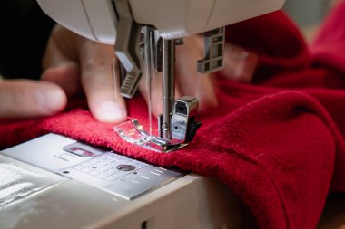 Kırmızı giysili bir dikiş makinesi kullanan bir adam. Tamir, kişiselleştirme, yaratma, yükseltme.
