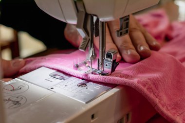 Pembe elbiseli bir dikiş makinesi kullanan bir adam. Tamir, kişiselleştirme, yaratma, yükseltme için.