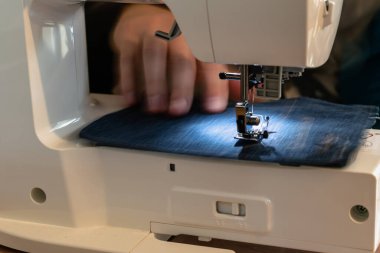 Mavi giysili dikiş makinesi kullanan bir adam. Tamir, kişiselleştirme, yaratma, yükseltme.