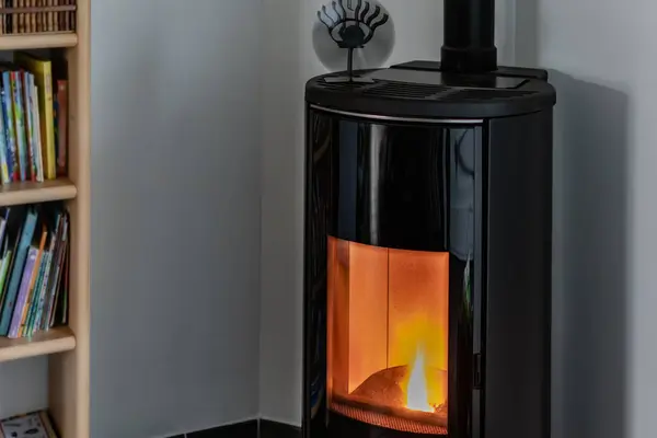 Kitaplık ve ısı dağıtıcısıyla oturma odasında ateşle yanan pelet sobası.