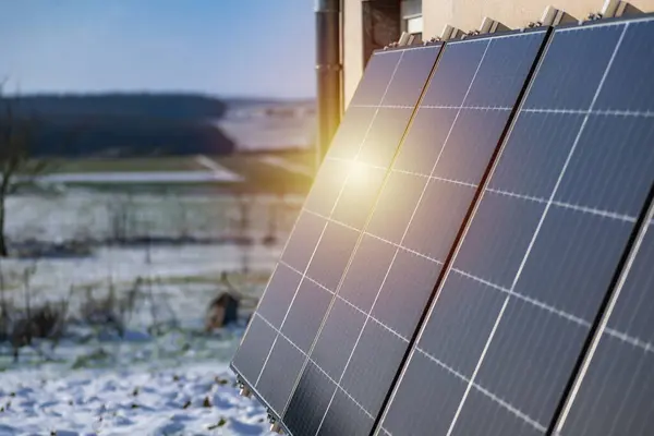 Solar panels with snow on ground on a well-exposed wall of an individual house, making savings following the energy crisis, eco-citizen gesture, green energy