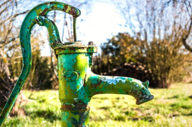 Old hand water pump on a well in the garden, watering and saving water, rural environnement