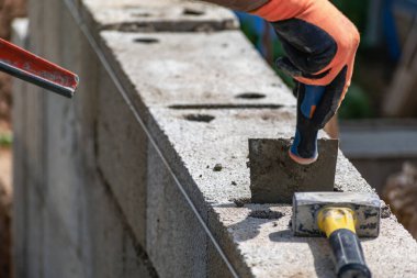 Bir tuğla ustası beton, mala, döşeme ve öğütücüyle inşaat sahasına duvar örmek için bloklar üzerinde çalışır.