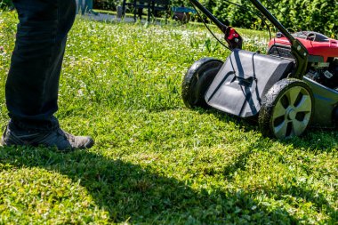 Bahçedeki bir makineyle çimleri biçiyor.