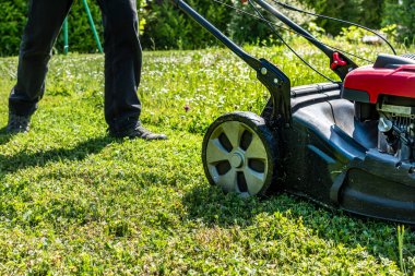 Bahçedeki bir makineyle çimleri biçiyor.