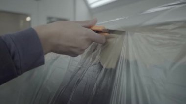 İşçi arabayı maskeliyor. Elini görebiliyorsunuz. Plastiği ağır çekimde kesiyor..