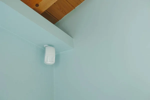 Motion sensor or detector for security system mounted on blue wall in mansard with wooden ceiling.