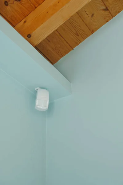 Motion sensor or detector for security system mounted on blue wall in mansard with wooden ceiling.