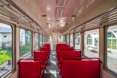 Boş, eski bir tren ya da tramvay vagonunun içi parlak kırmızı koltuklar ve geniş pencerelerle dolu.