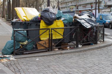 Paris 'teki büyük çöp konteynırları plastik poşetler ve çöp poşetleriyle dolu ve çöp tenekesi grevinin yanındaki metro istasyonunun yanındaki kaldırıma sıkışmış.