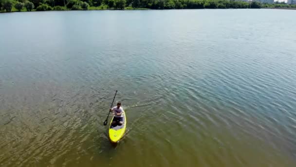 北ヨーロッパの美しい湖でSupボードをパドリングする若い男のドローンビュー Supボードのパドルを持つ男は ウクライナのシュミーの湖に浮かぶ — ストック動画