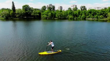 Kuzey Avrupa 'daki güzel bir gölde SUP sörfü yapan genç bir adamın insansız hava aracı görüntüsü. Sumy şehrinde Ukrayna 'da bir gölde jipli bir adam yüzüyor.