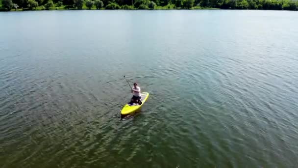 北ヨーロッパの美しい湖でSupボードをパドリングする若い男のドローンビュー Supボードのパドルを持つ男は ウクライナのシュミーの湖に浮かぶ — ストック動画