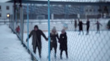 İnsanlar Kuzey Avrupa 'da bir hokey stadyumunda kayıyorlar. İnsanlar Sumy, Ukrayna 'daki buz pateni pistinde eğleniyor. Zincirli bir tel örgüden bak