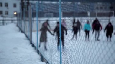 İnsanlar Kuzey Avrupa 'da bir hokey stadyumunda kayıyorlar. İnsanlar Sumy, Ukrayna 'daki buz pateni pistinde eğleniyor. Zincirli bir tel örgüden bak