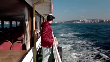 İstanbul 'daki bir teknenin güvertesinden şehrin manzarasına hayran olan bir adam, Trkiye. Boğaz gezisi. İstanbul 'da tekne gezisi, Trkiye. Teknede mutlu bir adam.