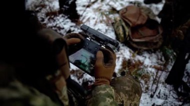 Askeri bir İHA operatörü askeri eğitim sahasında bir İHA 'yı kontrol ediyor. Kuzey Avrupa 'da kışları askerler ateşli silahlarla ateş ediyorlar. Askeri eğitim.