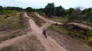 Exciting FPV drone chase of two motocross riders competing on a forest dirt track. Riders jump ramps, race at high speed, and showcase extreme motocross action from a cinematic aerial perspective