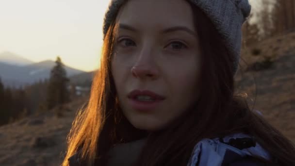 当一个女孩转身面对夕阳时 温柔地看着她的脸 傍晚时分 身后是白雪覆盖的春山脉 — 图库视频影像