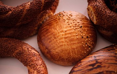 Simit ve üzerine susam tohumları konmuş yuvarlak somunlar da dahil olmak üzere taze pişmiş Türk ekmeklerinin yakın çekimi, altın kabuklarını ve davetkar dokularını ön plana çıkarıyor..