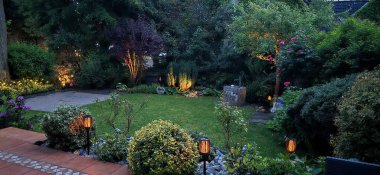 Gün batımında güneş enerjisiyle çalışan ışıklarla aydınlatılmış güzel bir ev bahçesi.