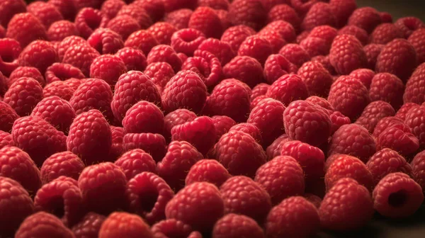 A stunning photograph of raspberries piled high on a seamless background. Each raspberry is highly detailed and adorned with glistening droplets of water. The low angle of the shot makes the viewer feel as though they are looking up at a towering pil
